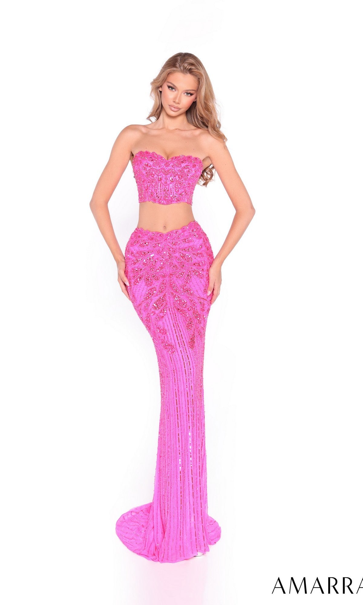 A woman models the Amarra 89059 Long Prom Dress—a stunning, form-fitting pink two-piece gown with a strapless top and sequin-embellished long skirt—standing out beautifully against the white background.